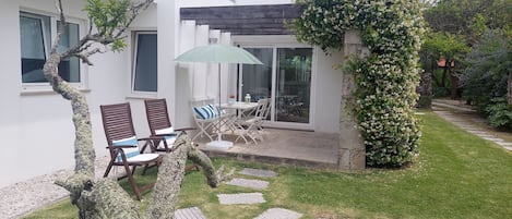 Ett modernt hus med en uteplats som har två trästolar, ett bord och ett grönt parasoll.