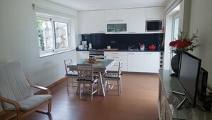 A modern kitchen with white cabinets, a dining table with chairs, and a TV on a stand.
