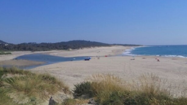 A beach with a clear sky, sandy shore, and a few people.