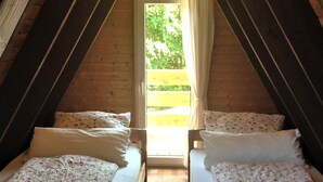 A small, cozy attic bedroom with two single beds, a red carpet, wooden beams, and a window with curtains.