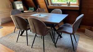 A dining area with a wooden table and four chairs, a window with blinds, and a television on the left.