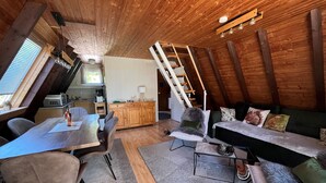 A cozy loft-style room with a dining area, a sofa, and a staircase leading to an upper level.
