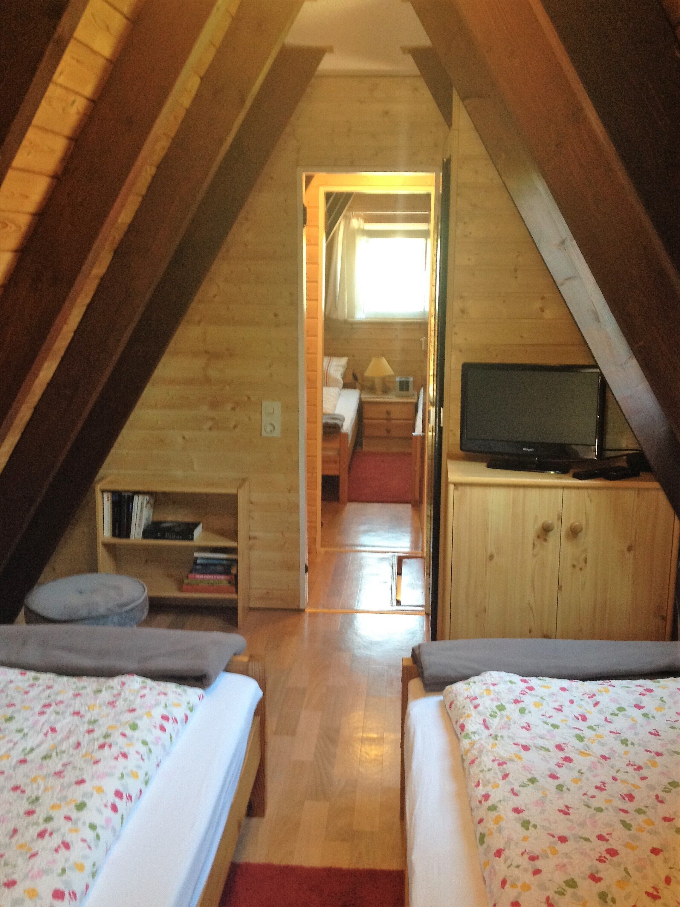A cozy attic bedroom with two beds, a TV, and a small bookshelf.