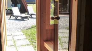A wooden interior with a door leading to an outdoor area with a patio and lounge chairs.