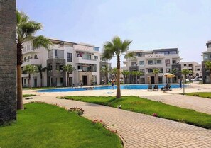 Guests can enjoy a refreshing swim in the central pool surrounded by lush lawns and palm trees.