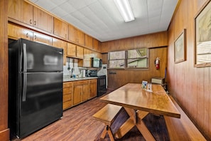 A kitchen with wooden cabinets, a black refrigerator, a wooden dining table, and a window with a view.