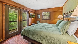 A bedroom with a large bed, a wooden door, and a view of a forest through the window.