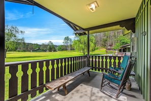 A porch with a bench and rocking chair, overlooking a green lawn and distant buildings.