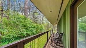 A wooden deck with a railing, a covered area, and a view of a forest.