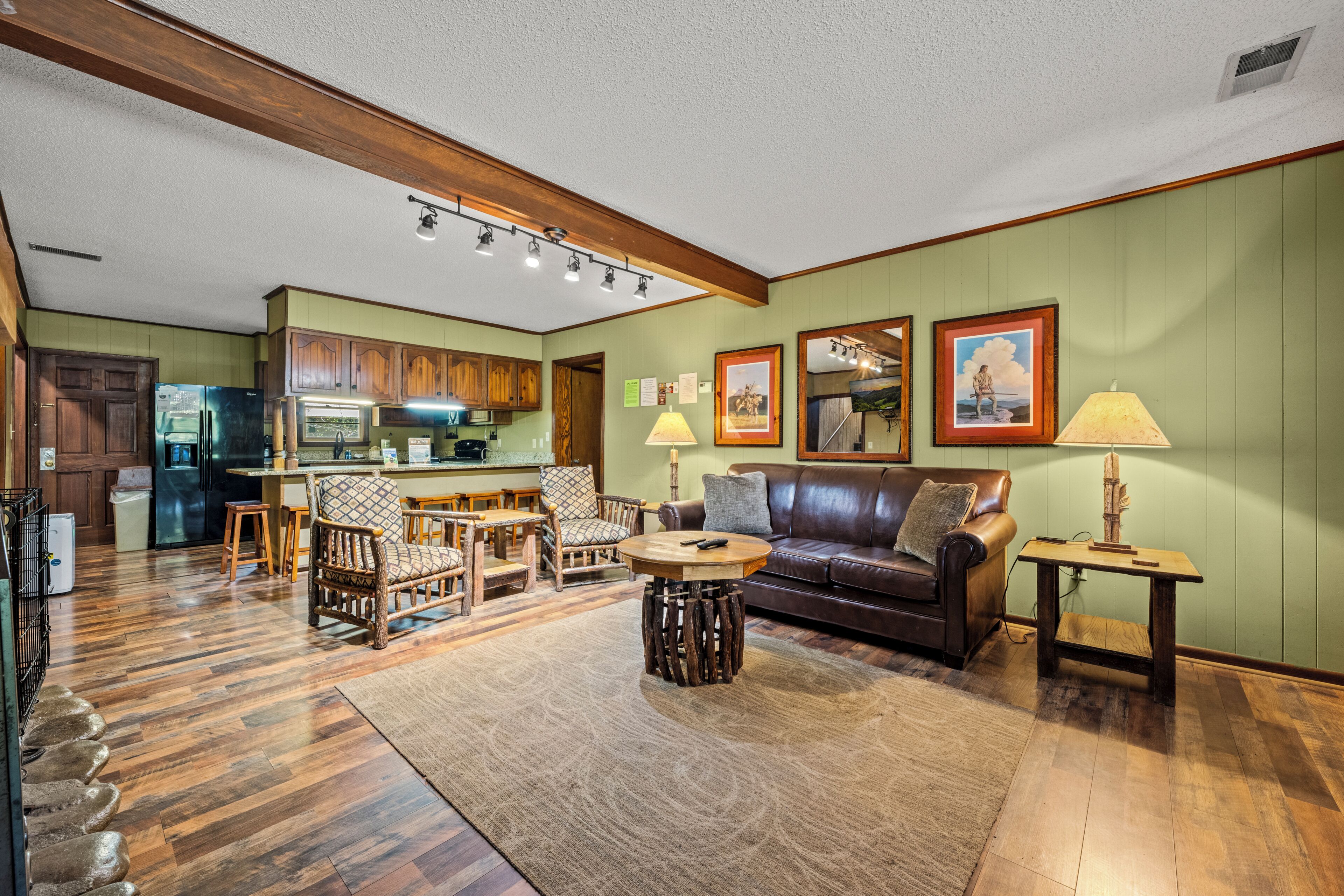 A spacious living area with a wooden floor, a leather sofa, a dining table, and a kitchen in the background.