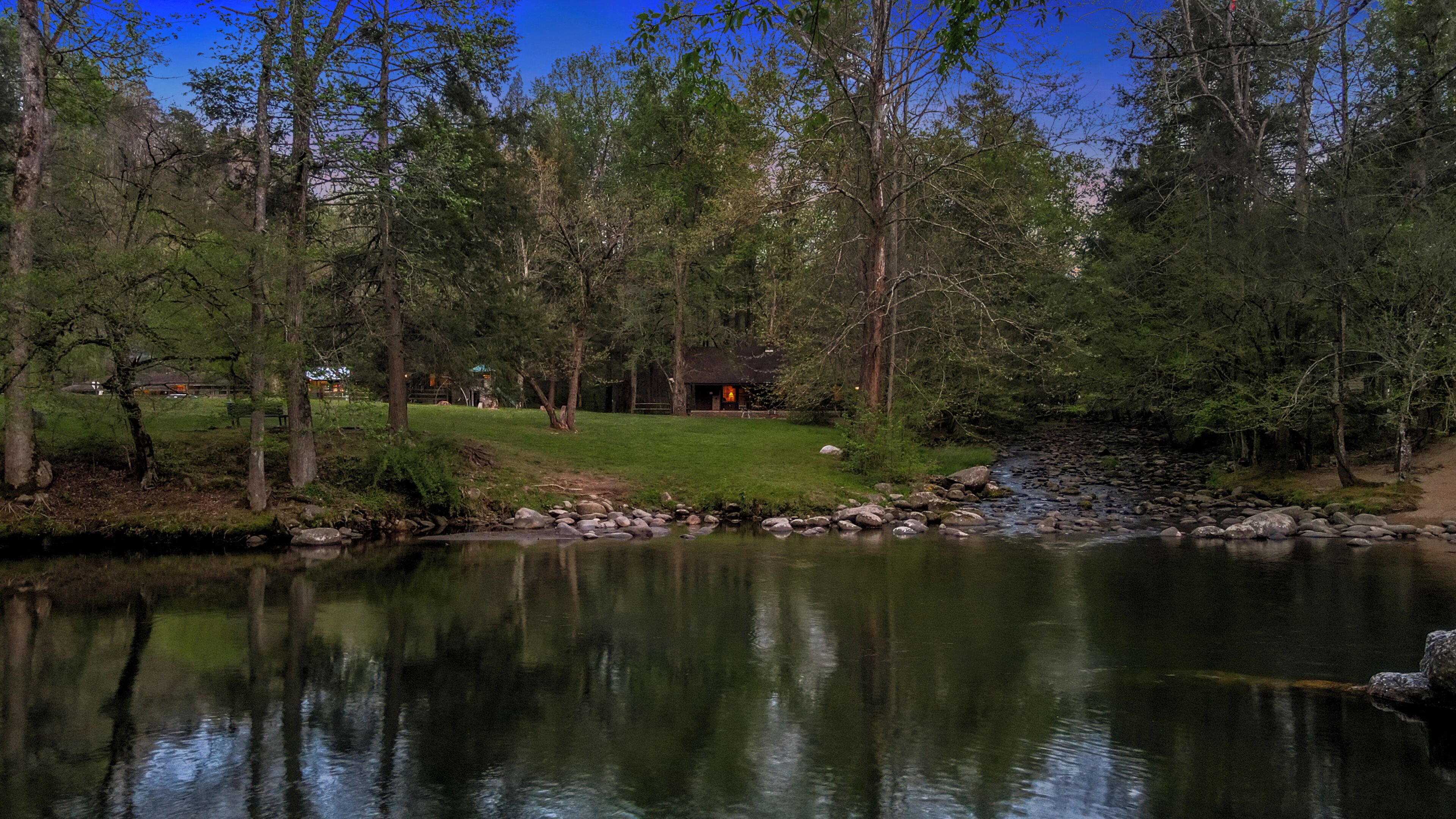 A lakeside cabin with a grassy area and a small stream.