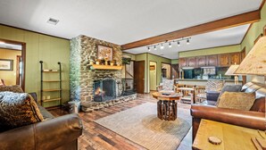 A living room with a stone fireplace, wooden flooring, a leather sofa, and a dining area with a table and chairs.