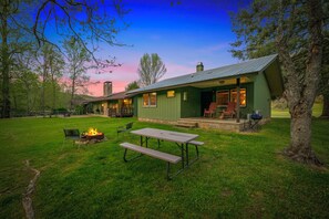 A green building with a patio area, a fire pit, and a picnic table.