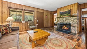 A wooden-paneled room with a stone fireplace, a sofa, a coffee table, and a television. - Riverside Cabin, minutes to Downtown Gatlinburg! Includes tickets to Dollywood, Anakeesta, (Sevierville)