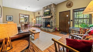 A cozy living room with a stone fireplace, wooden furniture, and large windows. - 3 Bedroom 2.5 miles from Rocky top sports complex (Sevierville)