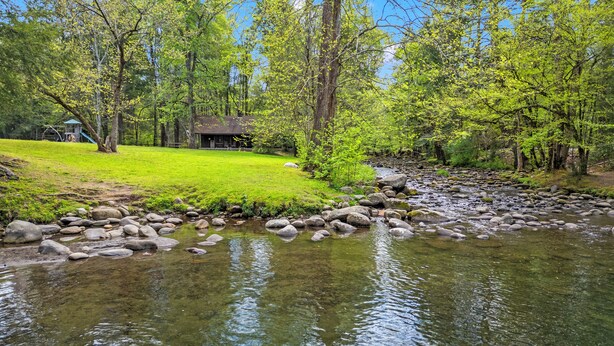 A river with rocks, a grassy area, and trees.