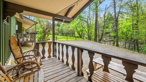 A wooden deck with a railing, chairs, and a view of a forested area.
