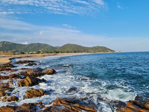 A coastal landscape with rocky shores, a sandy beach, and hills in the background.