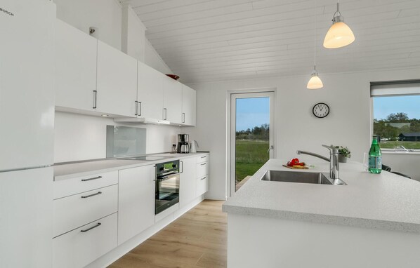A modern kitchen with white cabinetry, a built-in oven, a coffee maker, and a large window overlooking a green landscape. - Amazing home in Grenaa with WiFi (Grenaa)