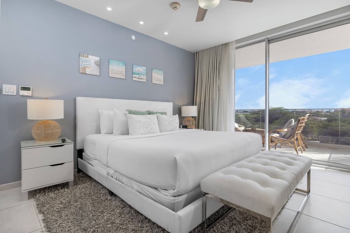 A modern bedroom with a large bed, bedside tables, and a view of the outdoors.