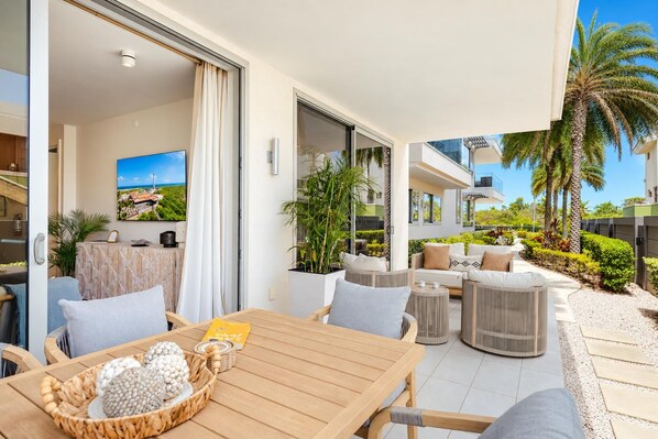 A modern outdoor patio with a wooden table, chairs, and a seating area with cushions.
