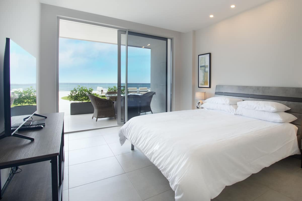 A modern hotel room with a large bed, a desk, and a balcony with a view of the ocean.