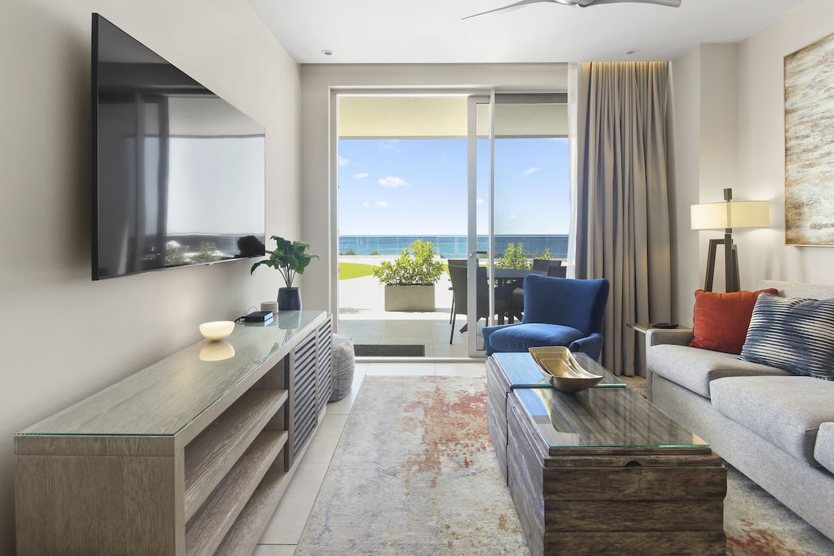 A modern hotel room with a large TV, a sofa, a coffee table, and a view of the ocean.