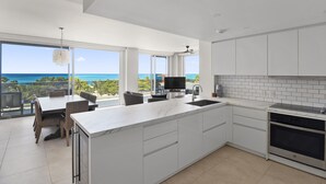 Una cucina moderna con un'isola grande, mobili bianchi e vista sull'oceano.