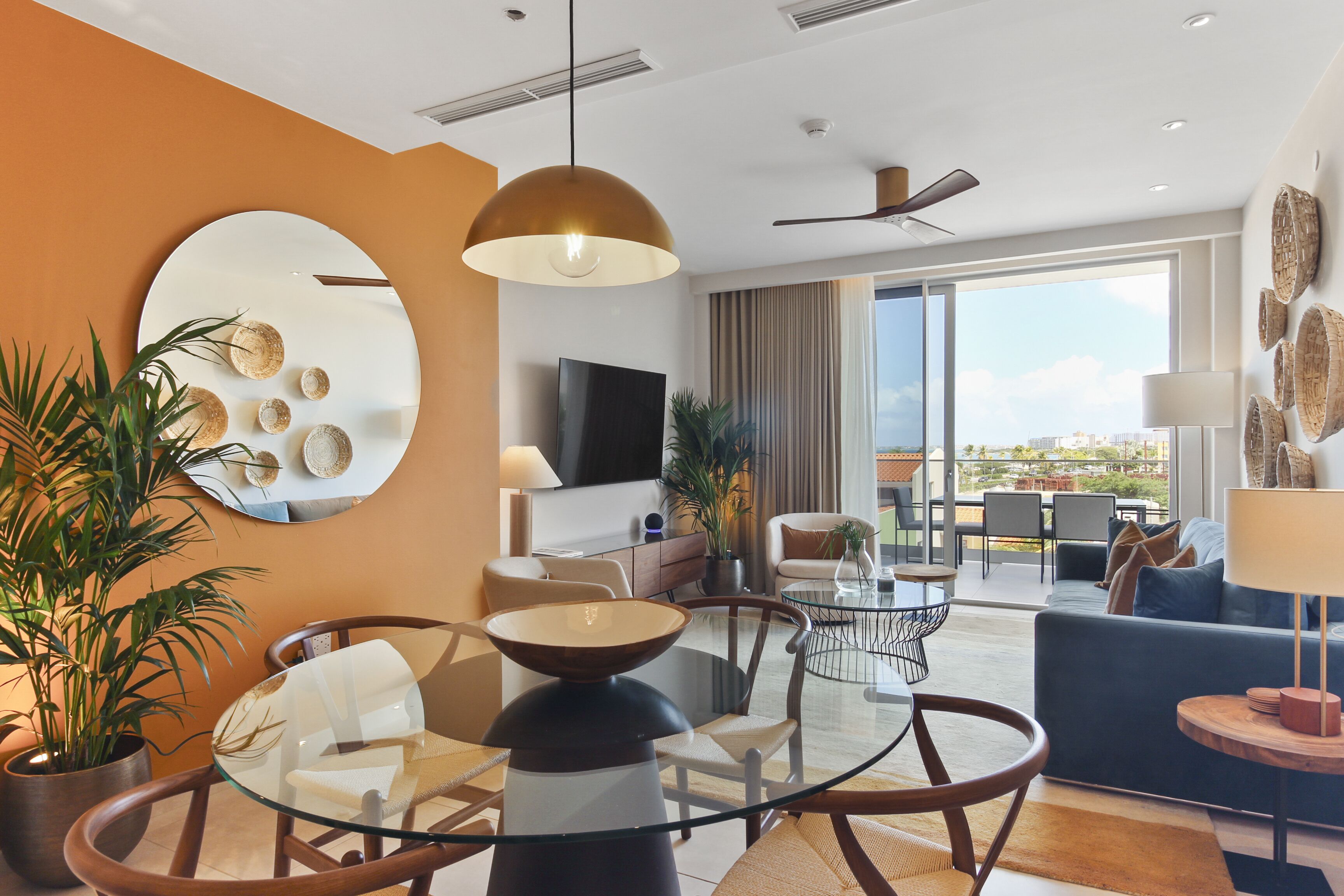 Una habitación de hotel moderna con una mesa de comedor de vidrio, un sofá, un televisor y un balcón con vistas.