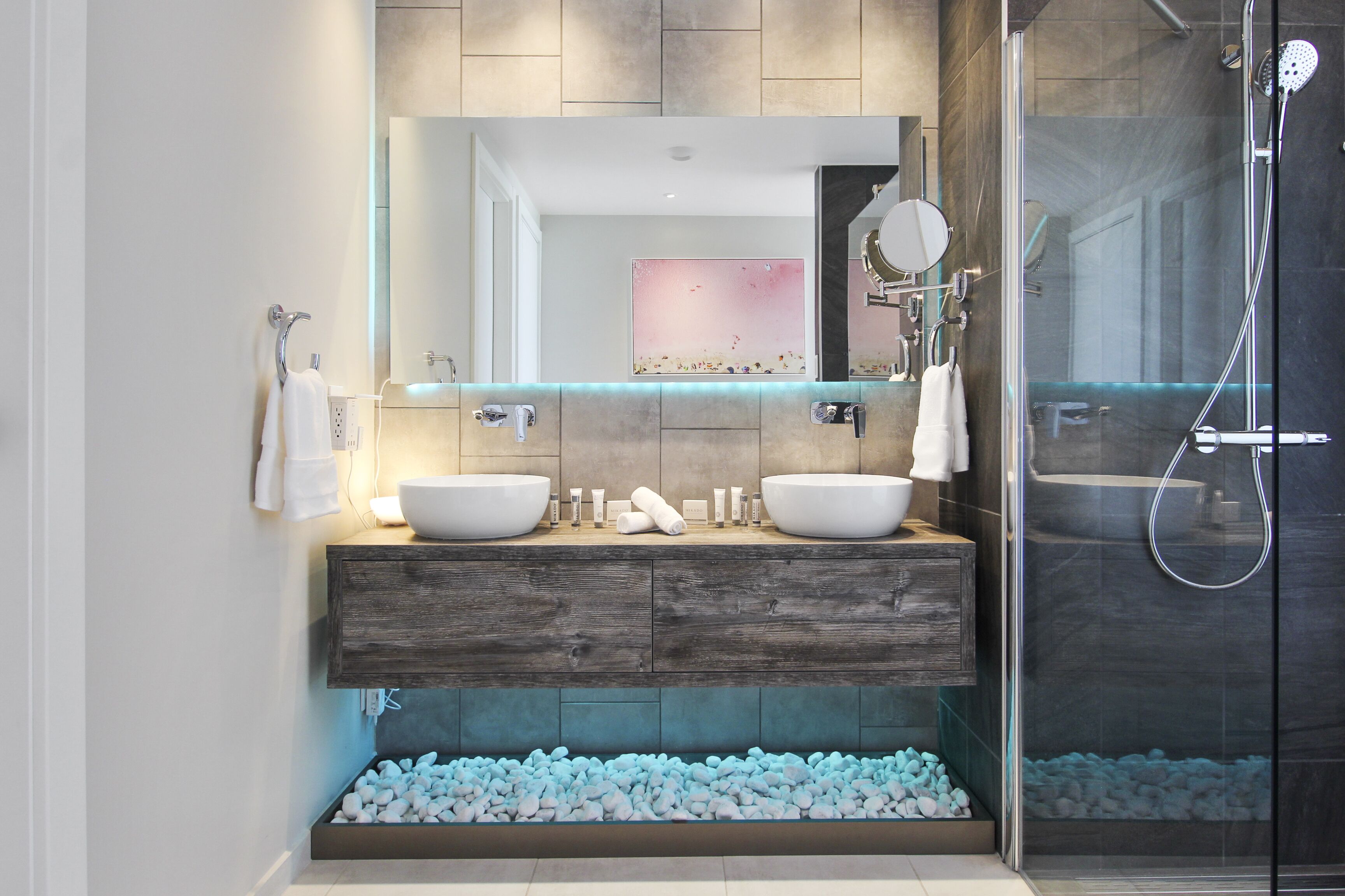 Une salle de bain moderne avec deux lavabos, un grand miroir et une douche à parois de verre.