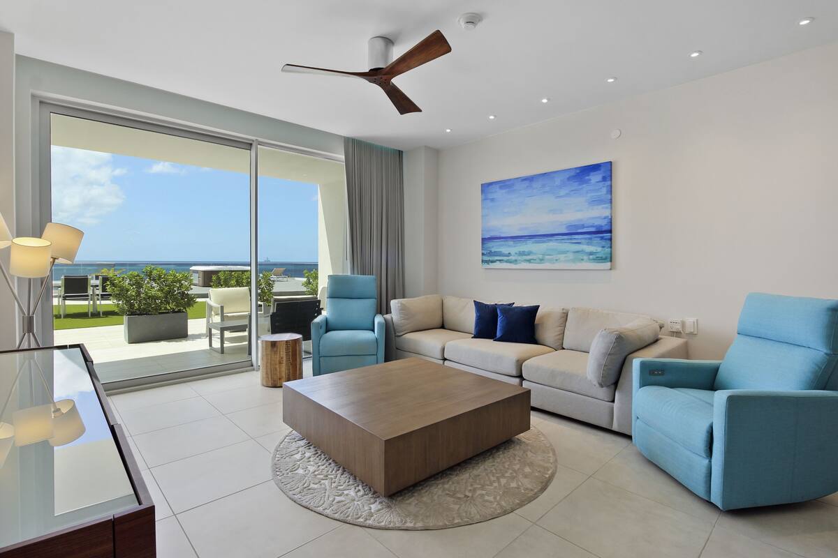 A modern living room with a glass coffee table, a beige sofa, and a blue armchair.