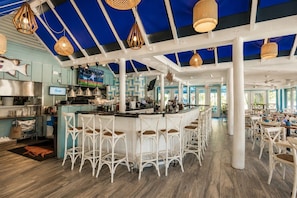 A restaurant with a bar area, white wicker chairs, and a blue and white color scheme.