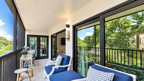 A balcony with a seating area, a table, and a view of greenery.