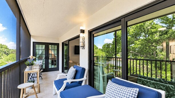 A balcony with a seating area, a table, and a view of greenery.