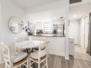 A modern kitchen with white cabinets, a stainless steel refrigerator, and a marble dining table with four chairs.