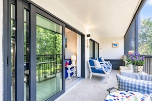 A balcony with a glass door, outdoor seating, and a view of greenery.