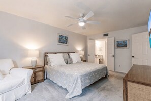 A bedroom with a bed, nightstands, a chair, a ceiling fan, and two doors.