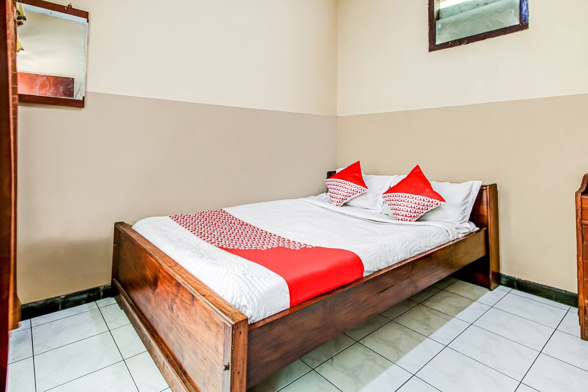 A neatly made bed with a wooden frame, white bedding, and red accents.