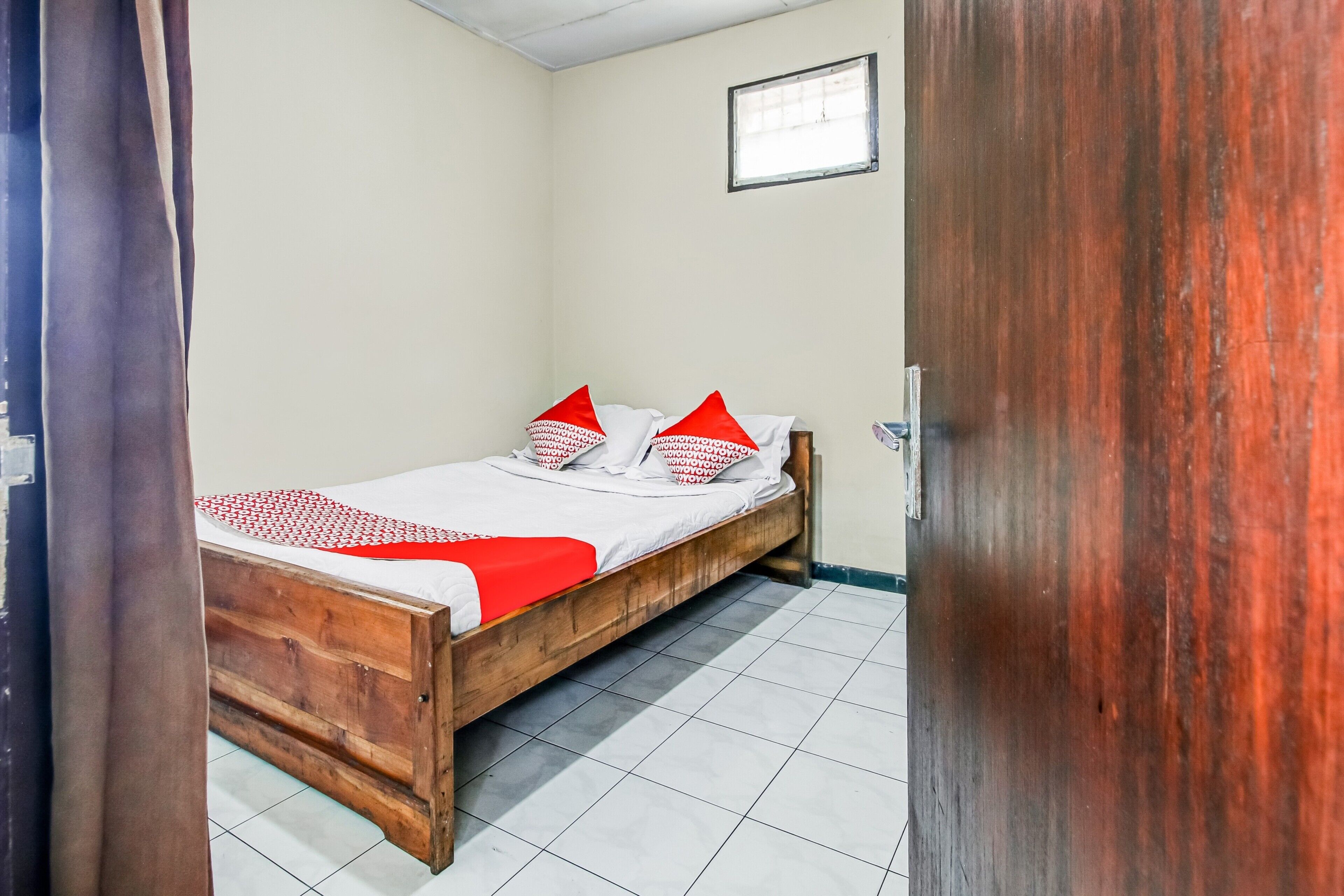 A bedroom with a wooden bed, white bedding, and red pillows.