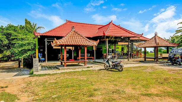 A traditional building with a red tiled roof, a covered seating area, and a parked scooter. - OYO 91053 Desa Wisata Gilimanuk (Malang)
