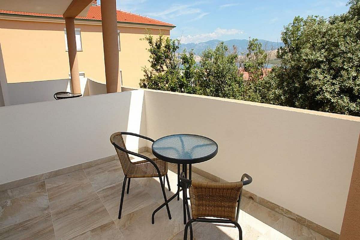 Un balcon avec deux fauteuils en osier et une petite table ronde, offrant une vue panoramique sur les arbres et les montagnes.