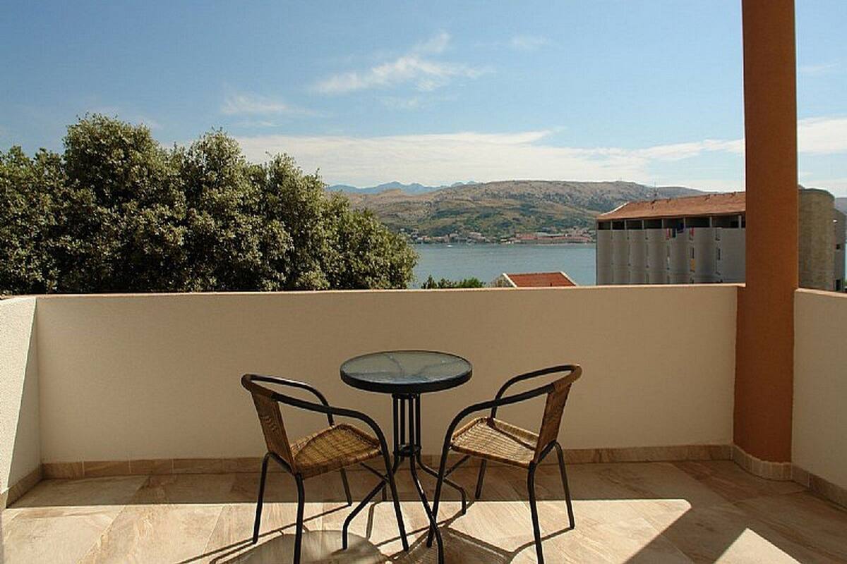 Un balcon avec deux fauteuils en osier et une petite table ronde, d’où l’on peut admirer un plan d’eau et des collines lointaines.