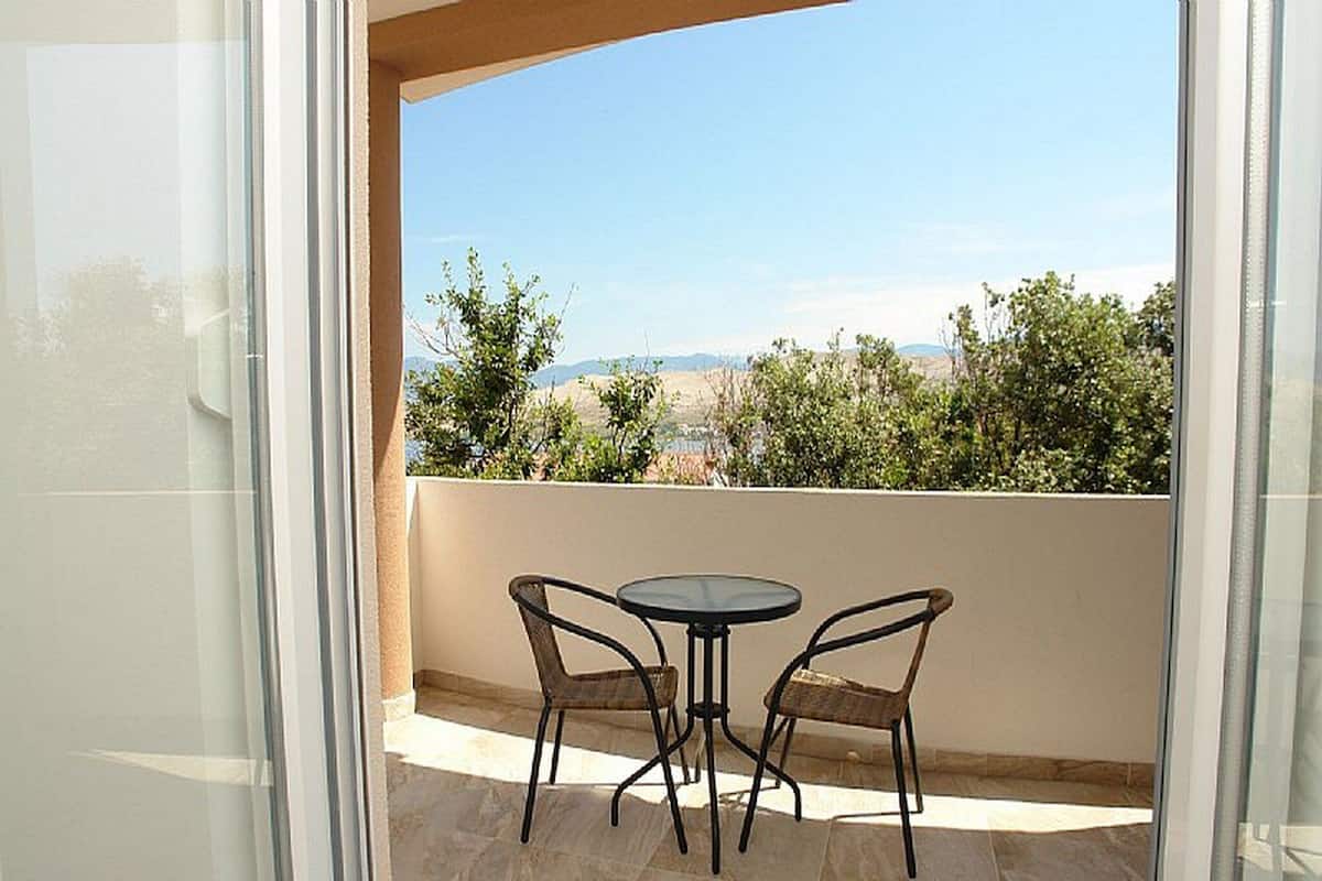 Un balcon avec une table et deux chaises, offrant une vue sur un paysage composé d’arbres et de collines lointaines.