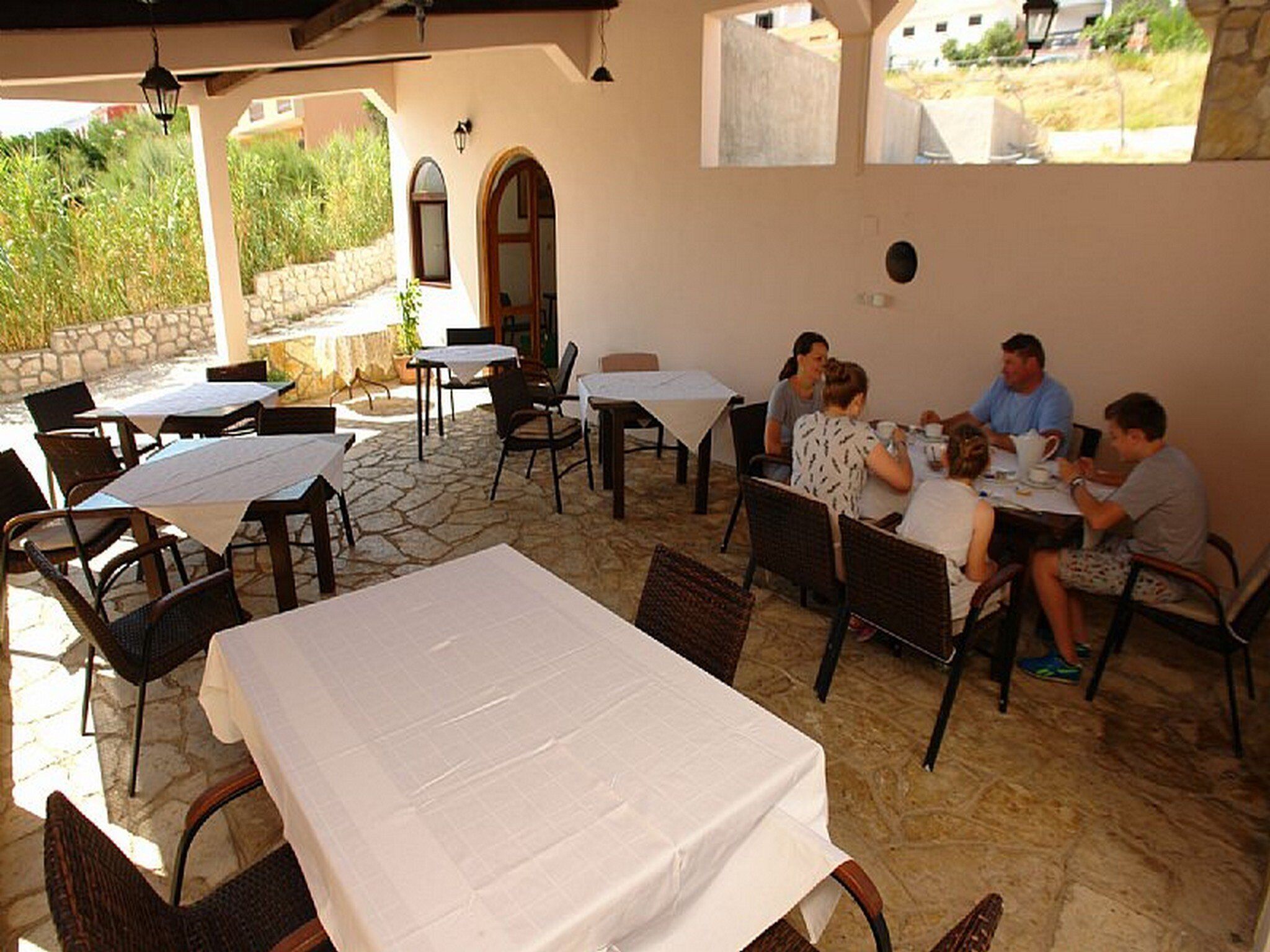 An outdoor dining area with stone flooring, tables with white tablecloths, and wicker chairs.