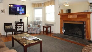 A living room with a flat-screen TV, a fireplace, a ceiling fan, and a cozy seating area. - Team Elm (Entire Property) (Oneonta)