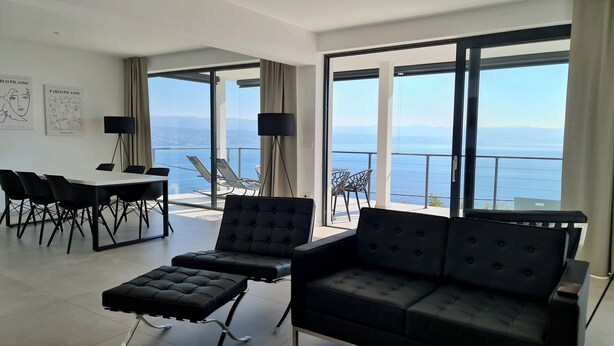 A modern living room with a large window, a sofa, a coffee table, and a dining area with chairs and a table.