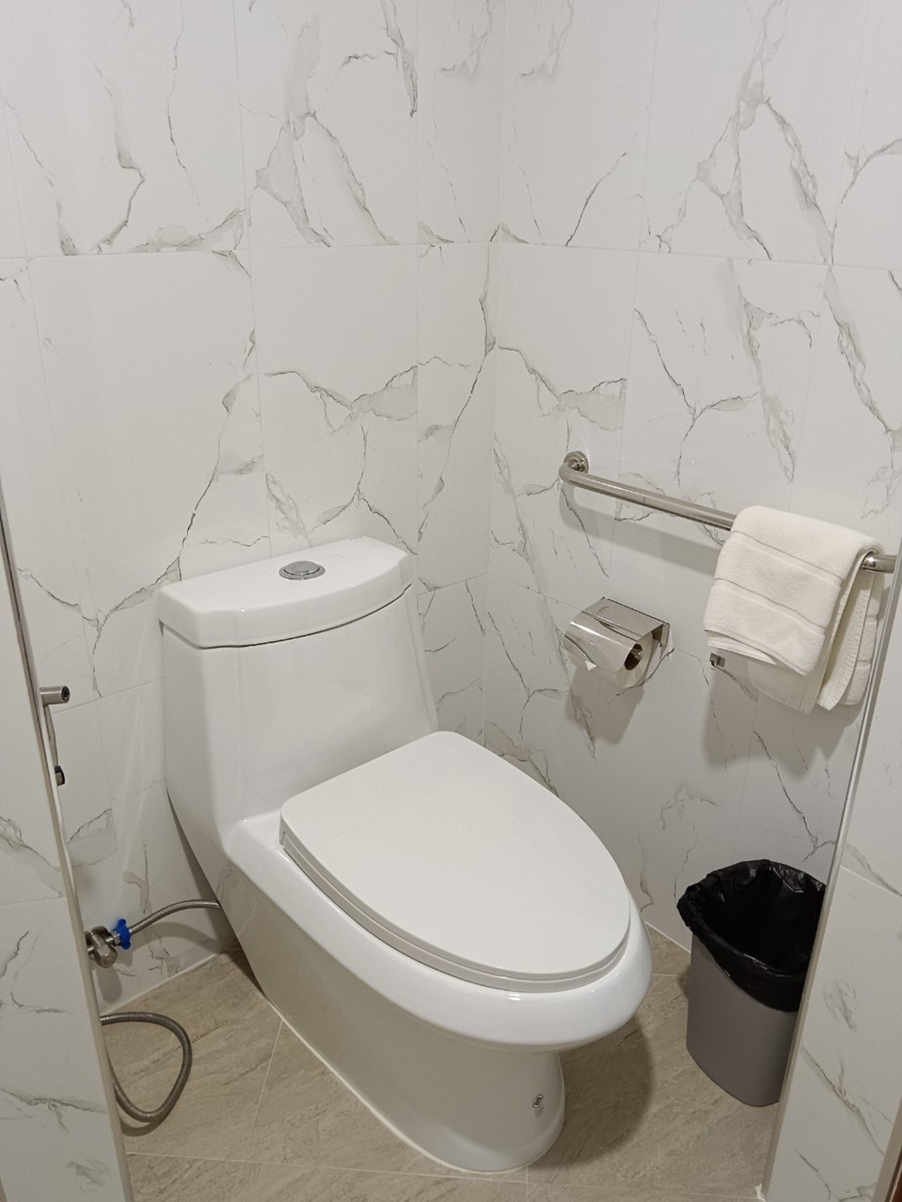 A bathroom with a toilet, a towel rack, and a trash bin.