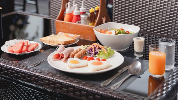 A dining area with wicker furniture, a table set with plates of food, a bowl of salad, and glasses of juice. - Baan Plaifah Khao Yai Hotel (Pak Chong)