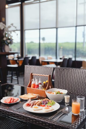 Un comedor con mobiliario de mimbre, una mesa dispuesta con platos de comida, un bol de ensalada y vasos de jugo.