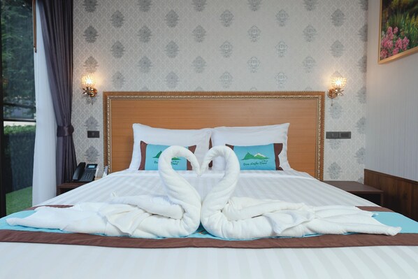 Una cama bien hecha con dos toallas dispuestas en forma de cisne, un cabecero de madera y una mesita de noche con un teléfono.